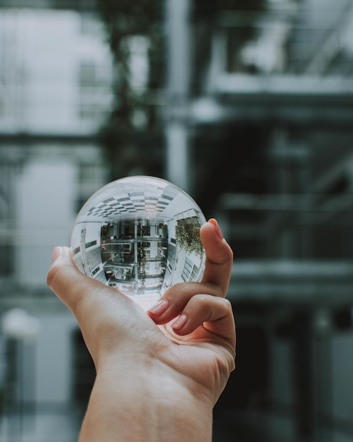 Gratis foto een persoon die een heldere kristallen glazen bol met de reflectie van een gebouw