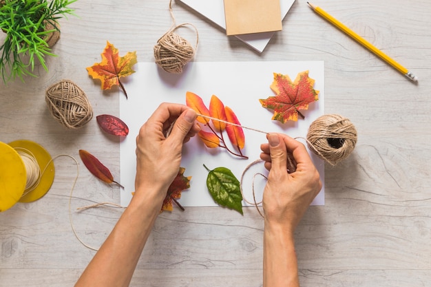 Gratis foto een persoon die koord met valse de herfstbladeren op houten achtergrond gebruikt