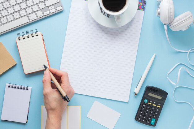 Een persoon die op blocnote met pen op bureau blauw bureau schrijft