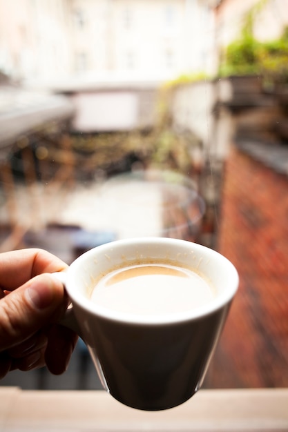 Een persoon hand houden kopje koffie nadenken over vensterglas