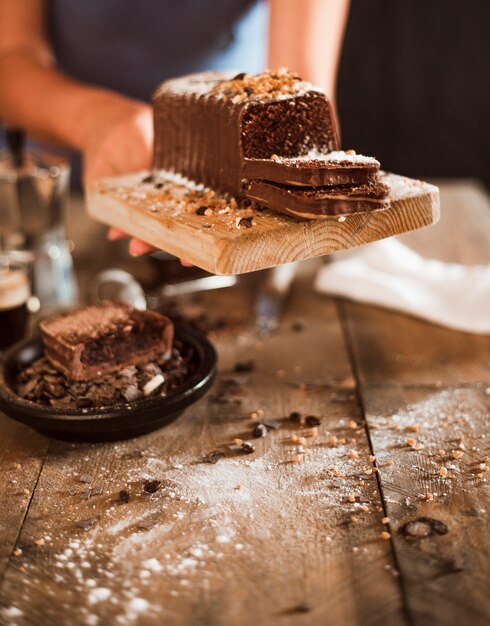 Een persoon hand met plakje cake op snijplank