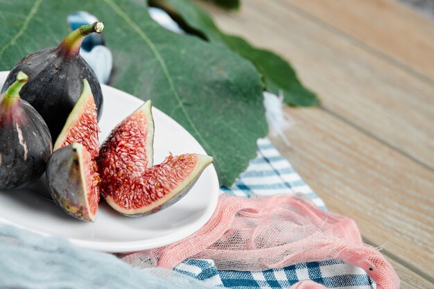 Een plaat van hele en gesneden zwarte vijgen met blauwe en roze tafelkleden op houten tafel.