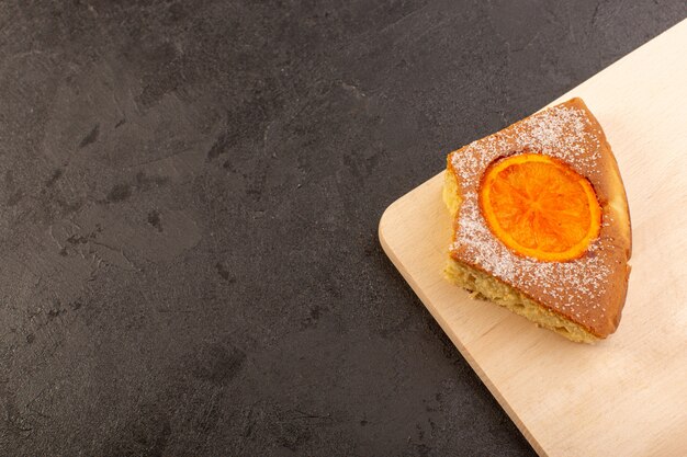 Een plak zoete zoete smakelijk van de hoogste menings oranje cake plak op het bruine houten bureau en een grijze achtergrond zoet suikerkoekje