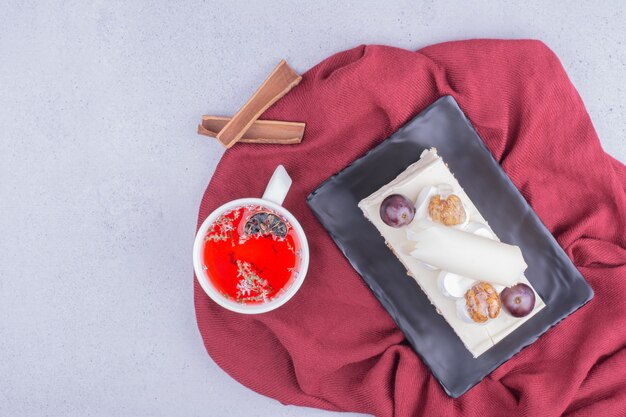 Een plakje cake in een keramische schotel met een kopje rode kruidenthee.