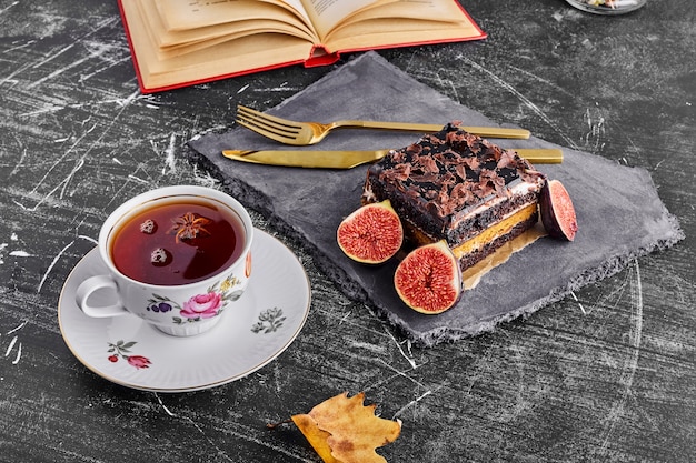 Een plakje chocoladetaart met vijgen en thee op een stenen schaal.