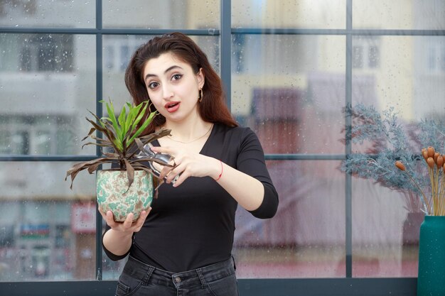 Gratis foto een portret van een jonge dame staat de bloempot water te geven en kijkt naar de camera