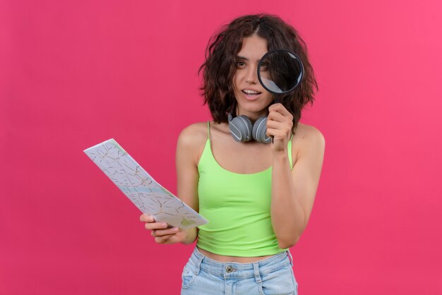 Een positieve jonge mooie vrouw met kort haar in een groene crop top in koptelefoon met vergrootglas