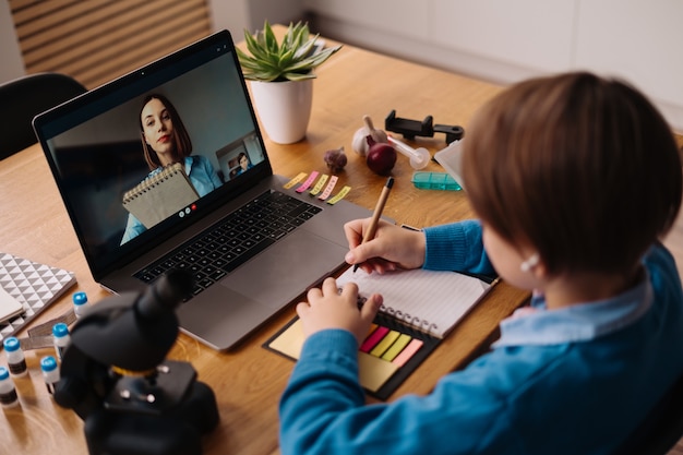 Een Preteen-jongen gebruikt een laptop om een videogesprek te voeren met zijn leraar