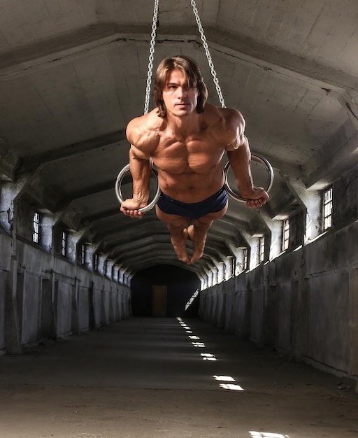 Een professionele atleet met een mooi gespierd lichaam traint op gymnastiekringen in een verlaten industrieel gebouw