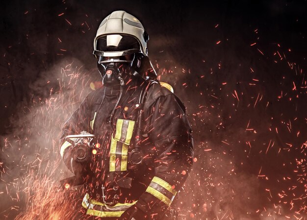 Een professionele brandweerman gekleed in uniform en een zuurstofmasker staande in vuurvonken en rook op een donkere achtergrond.