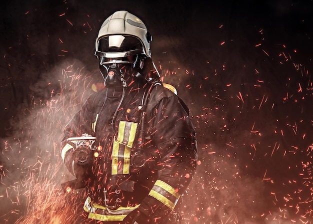 Een professionele brandweerman gekleed in uniform en een zuurstofmasker staande in vuurvonken en rook op een donkere achtergrond.