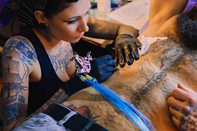 Gratis foto een professionele vrouwelijke tatoeëerder maakt zwart-witte tatoeage op bebaarde mannelijke torso in een salon.