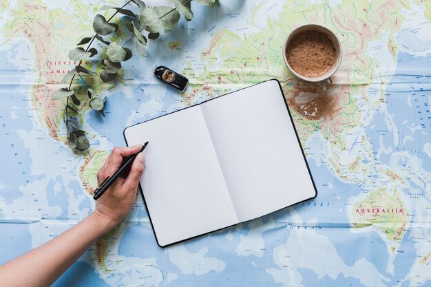 Een reiziger die op leeg notitieboekje met autostuk speelgoed schrijft, koffie over de kaart