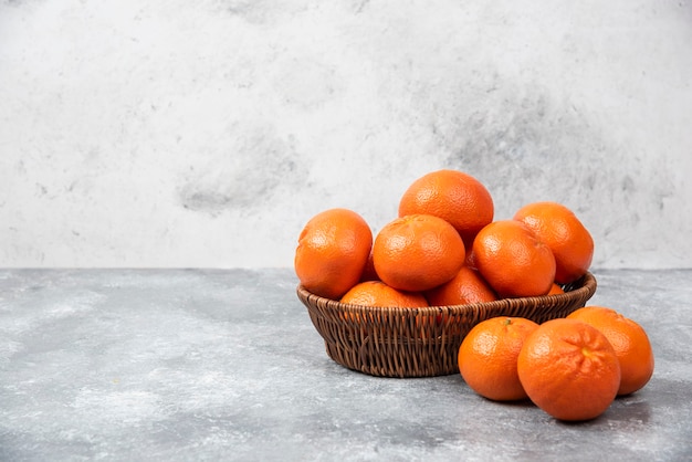 Een rieten doos vol sappig oranje fruit op stenen tafel.