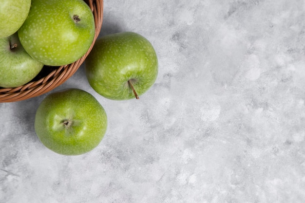 Een rieten mand met verse groene appels op steen