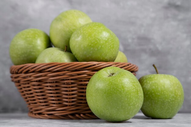 Een rieten mand met verse groene appels op steen