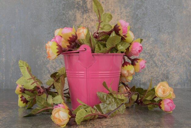 Een roze emmer met boeket bloemen op marmeren ondergrond.