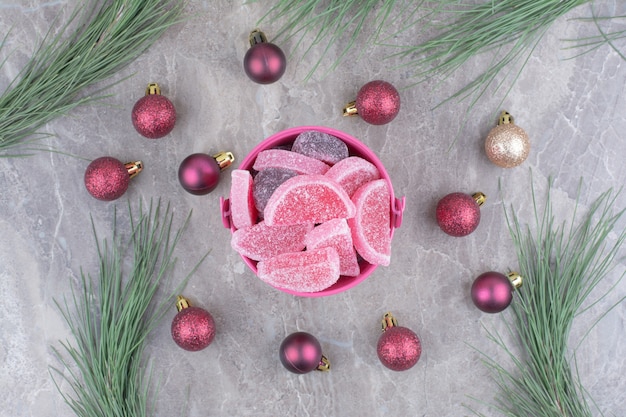 Een roze emmer vol zoete marmelades met rode kerstballen op marmeren achtergrond.