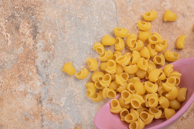 Een roze kom onvoorbereide macaroni op marmeren ruimte.