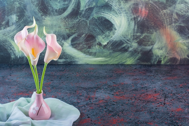 Gratis foto een roze vaas vol calla bloemen op tafelkleed.