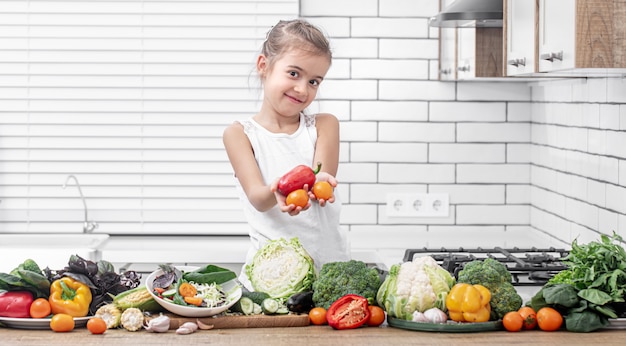 Een schattig klein meisje houdt verse groenten vast tijdens het voorbereiden van een salade kopie ruimte.