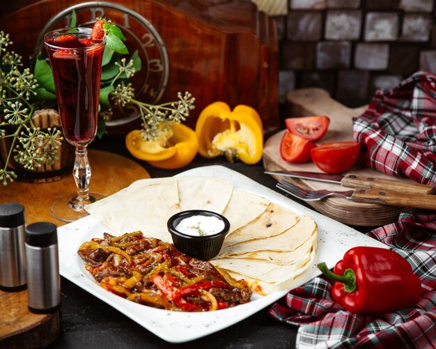 Een schotel fajitas van rundvlees geserveerd met flatbread en saus