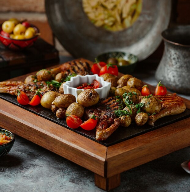 Een schotel van gegrild rundvlees, aardappelen en groenten op een stenen tafel