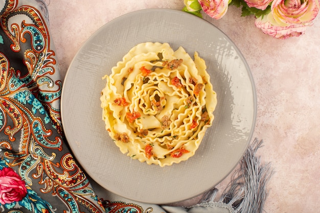 Een smakelijke maaltijd van bovenaanzicht Italiaanse pasta met gekookte groenten en kleine plakjes vlees binnen grijze plaat op kleurrijke sjaal en roze