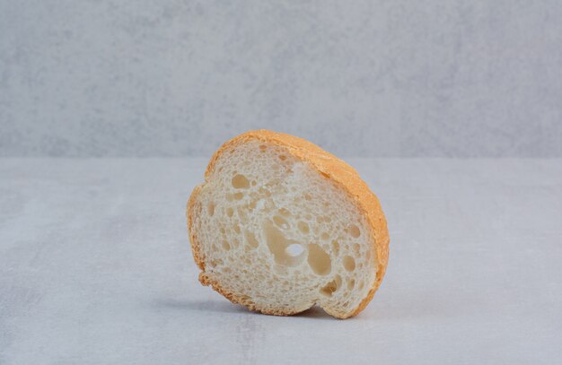 Een sneetje rond vers wit brood op marmeren achtergrond.