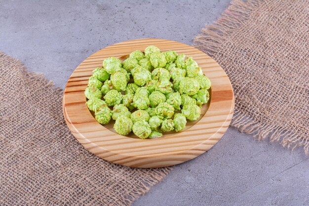 Een stapel groene gekonfijte popcorn op een houten schotel bovenop stukken doek op marmeren achtergrond. Hoge kwaliteit foto