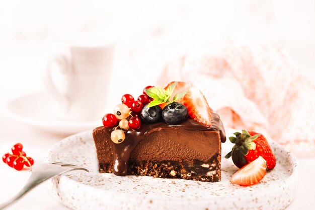 Een stuk chocolade cheesecake versierd met verse kersen, bosbessen en een kopje koffie op een beige achtergrond. Detailopname. Horizontaal