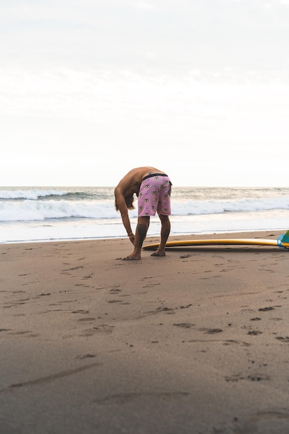 Een surfer loopt met een plank op een zandstrand. Knappe jonge man op het strand. watersport. Gezonde actieve levensstijl. surfen. Zomervakantie. Extreme sporten.