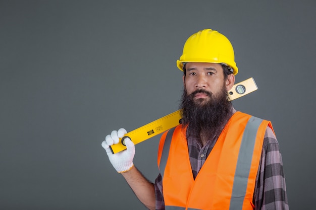 Een technische man die een gele helm draagt die een waterspiegelmeter op grijs houdt.