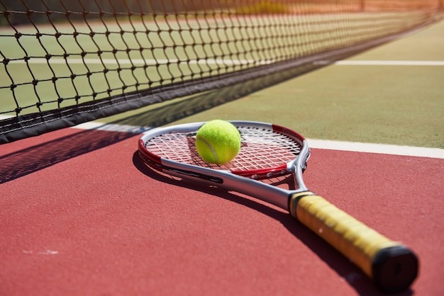 Een tennisracket en een nieuwe tennisbal op een pas geschilderde tennisbaan.