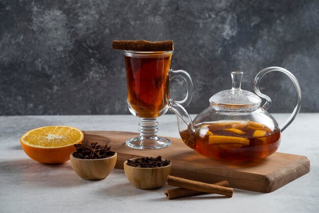 Een theepot met thee en een schijfje sinaasappel op een houten bord.