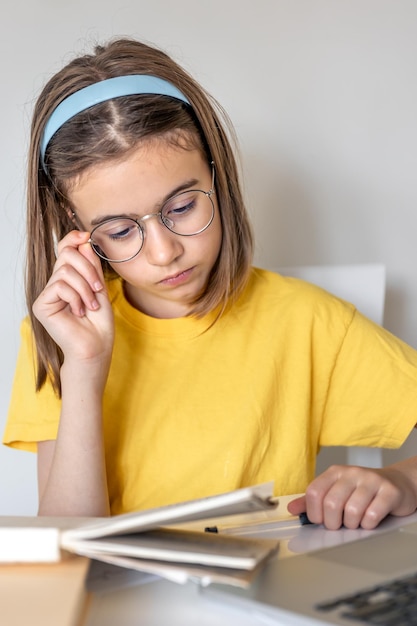 Een tienermeisje doet huiswerk met boeken en een laptop aan een tafel