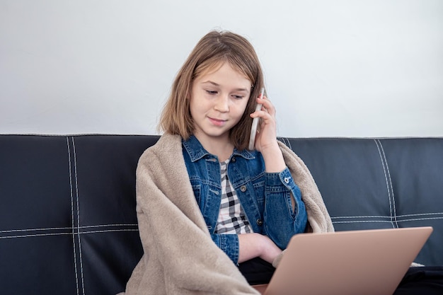 Een tienermeisje zit op de bank achter een laptop en praat aan de telefoon