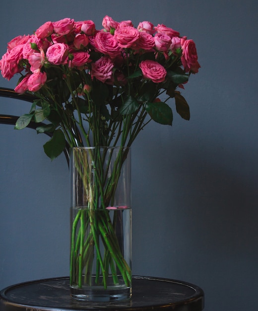 Een vaas met roze rozen die zich op een oude rustieke ronde poefstoel bevinden