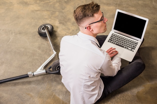 Een verhoogde weergave van de laptop in de hand zittend op de vloer van de jonge man