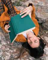Gratis foto een verhoogde weergave van een vrouwelijke wandelaar ontspannen op rots lezen van het boek