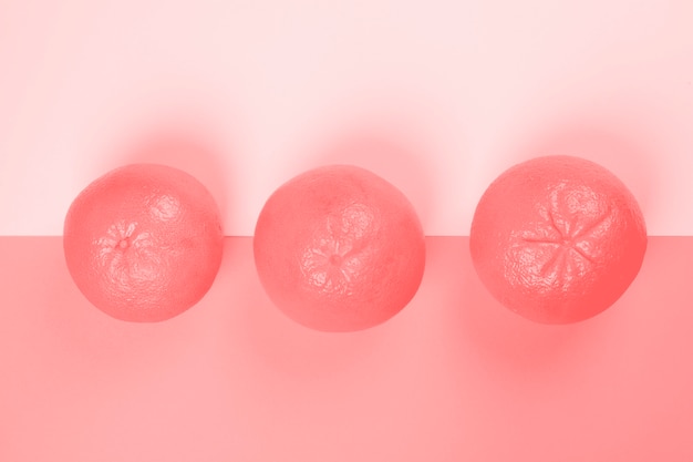 Een verhoogde weergave van hele drie grapefruit op roze achtergrond