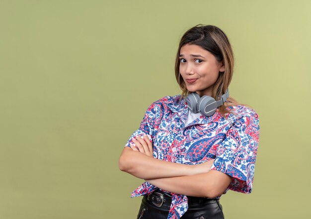 Een verwarde jonge vrouw met lang haar in een paisley bedrukt overhemd met een koptelefoon, hand in hand gevouwen