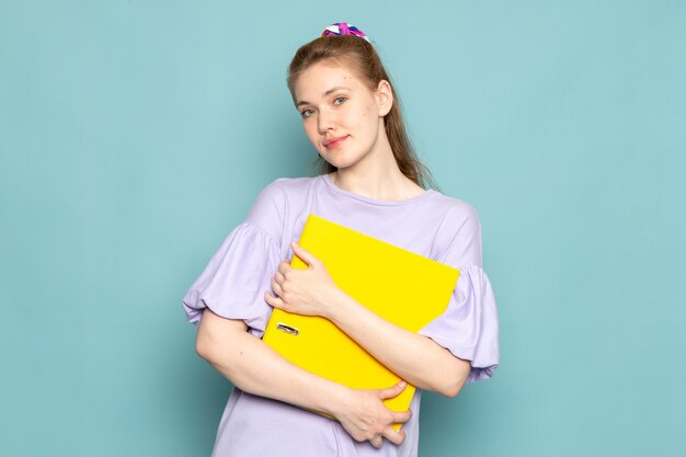 Een vooraanzicht aantrekkelijke vrouw in blauwe hemd-jurk met gele bestanden op blauw