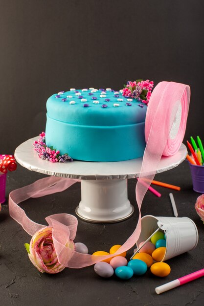 Een vooraanzicht blauwe verjaardagstaart met snoepjes en kaarsen op de donkere partij van de de cakeviering van de bureauverjaardag