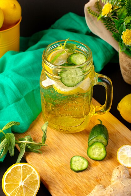 Een vooraanzicht citroen cocktail vers koel drankje in glazen beker gesneden en hele citroenen komkommers samen met bloemen op de donkere achtergrond cocktail fruit drinken