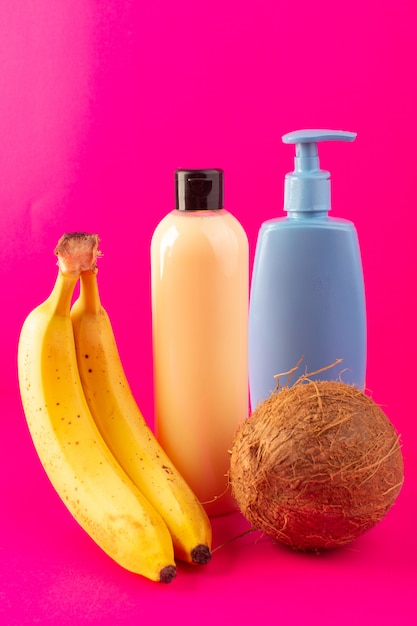 Gratis foto een vooraanzicht crèmekleurige fles plastic shampoo kan met zwarte dop geïsoleerd samen met bananen blauwe buis en kokosnoot op de roze achtergrond cosmetica schoonheid haar