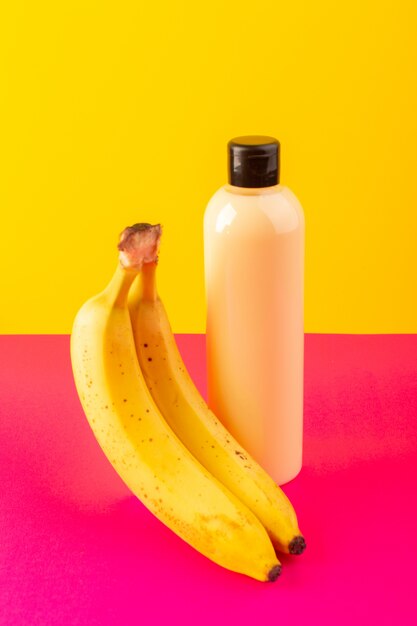 Een vooraanzicht crèmekleurige fles plastic shampoo kan met zwarte dop geïsoleerd samen met bananen op de roze-gele achtergrond cosmetica schoonheid haar