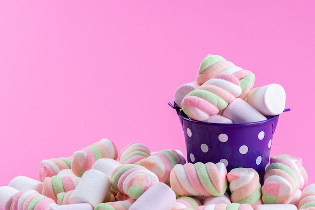 Een vooraanzicht dat marshmallows kauwt in een paarse beker en alles op roze, kleurenregenboogsuikerconfituur