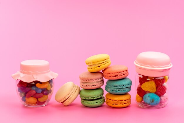 Een vooraanzicht Franse macarons kleurrijk samen met veelkleurige snoepjes in blikjes op roze, cake biscuit banketbakkerij