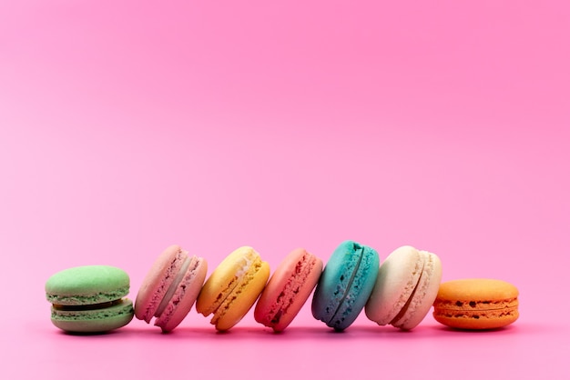 Een vooraanzicht franse macarons om heerlijk kleurrijk geïsoleerd op roze, cakekoekje banketbakkerij